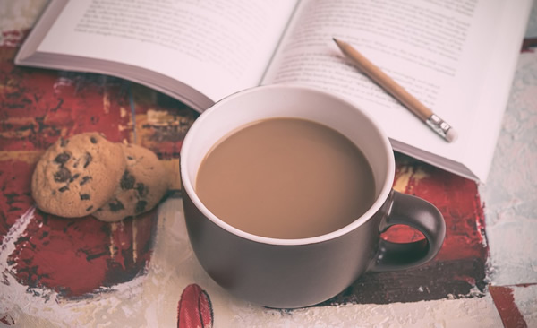 photo of a journal laying on a table with a pencil, cup of coffee, and cookies